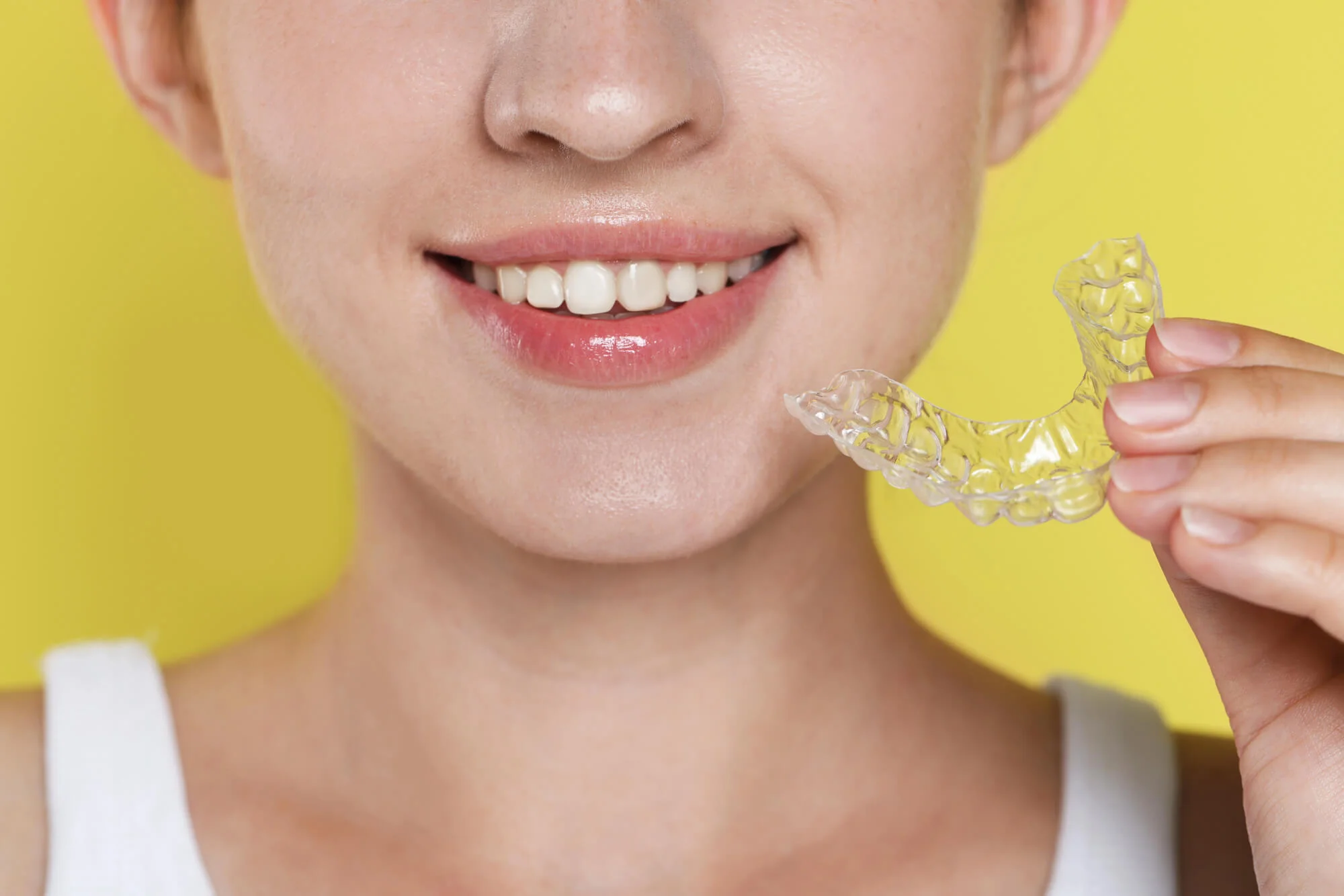 A teen girl holding an Invisalign-mandibular-advancement-aligner-on-a-yellow-background.