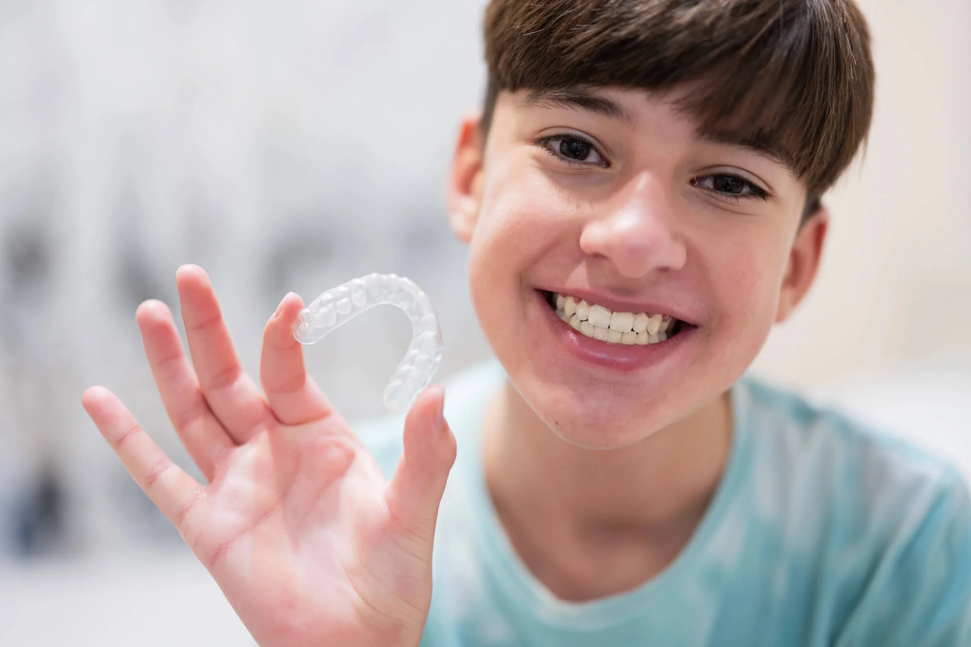 A teenage boy holding Invisalign-mandibular-advancement-clear-orthodontic-aligners.